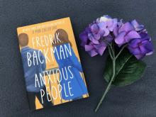 The Book, Anxious People by Fredrik Backman and a purple flower beside the book