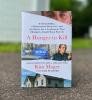 The book "A Hunger to Kill" by Kim Mager sitting on a sidewalk with a grass background